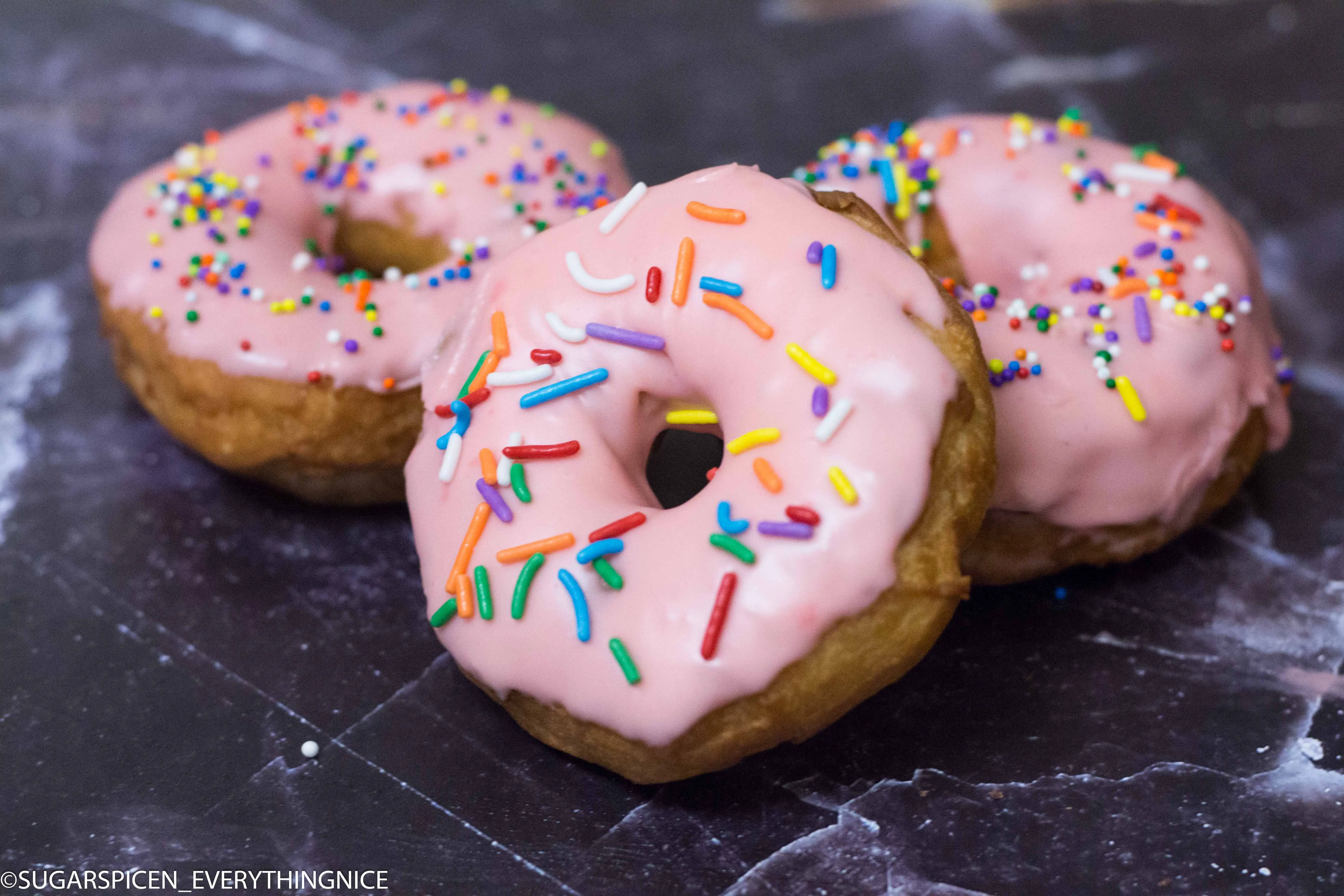 3 eggless donuts with pink chocolate glaze and sprinkles on top