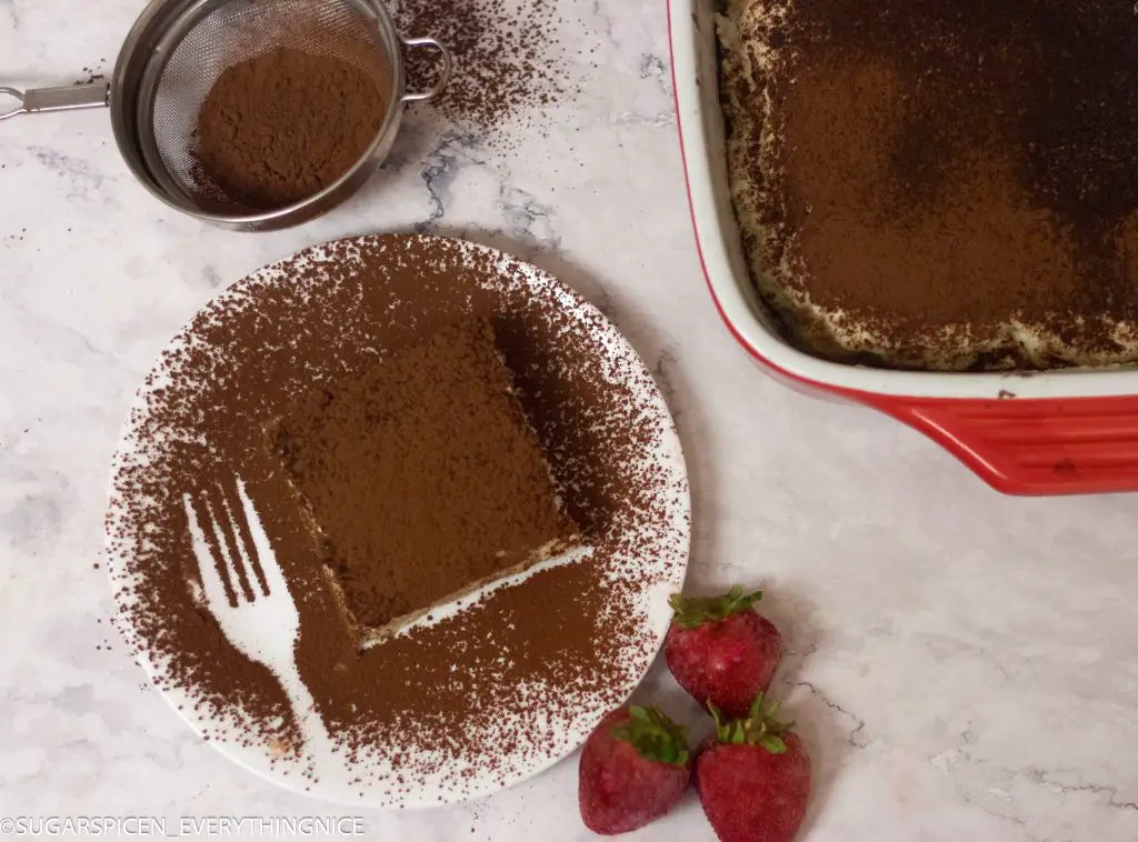 Eggless tiramisu covered in cocoa powder and 3 strawberries kept on the side