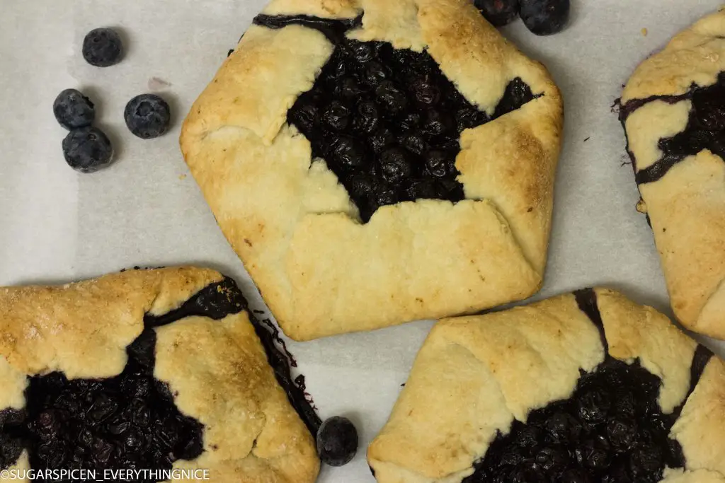 3 blueberry galettes with few blueberry around it placed on white marble countertop.