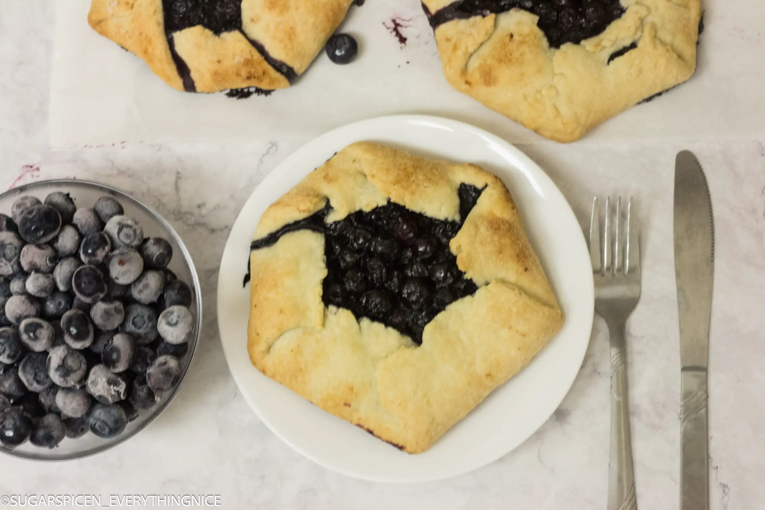3 blueberry galettes with few blueberries kept on a bowl.