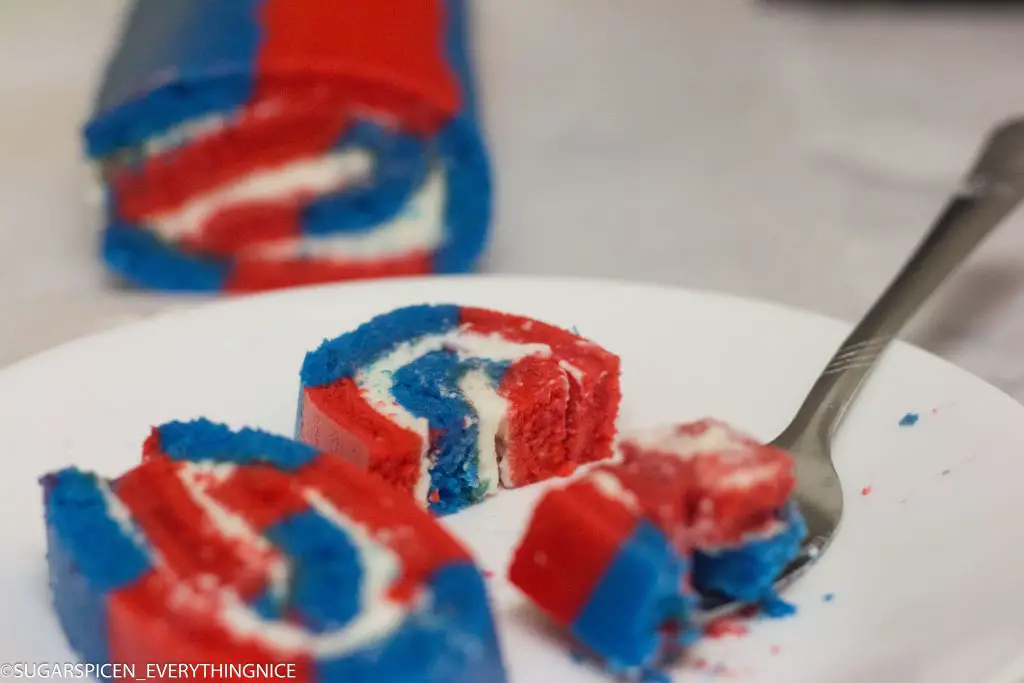 Swiss Rolls made with red and blue batter and whipped cream filling. One swiss roll piece is broken with the fork