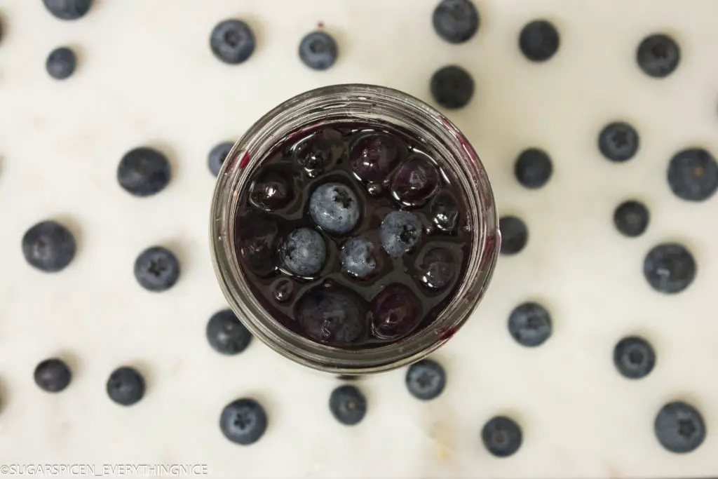 Top view of blueberry topping sauce and lot of blueberries around it