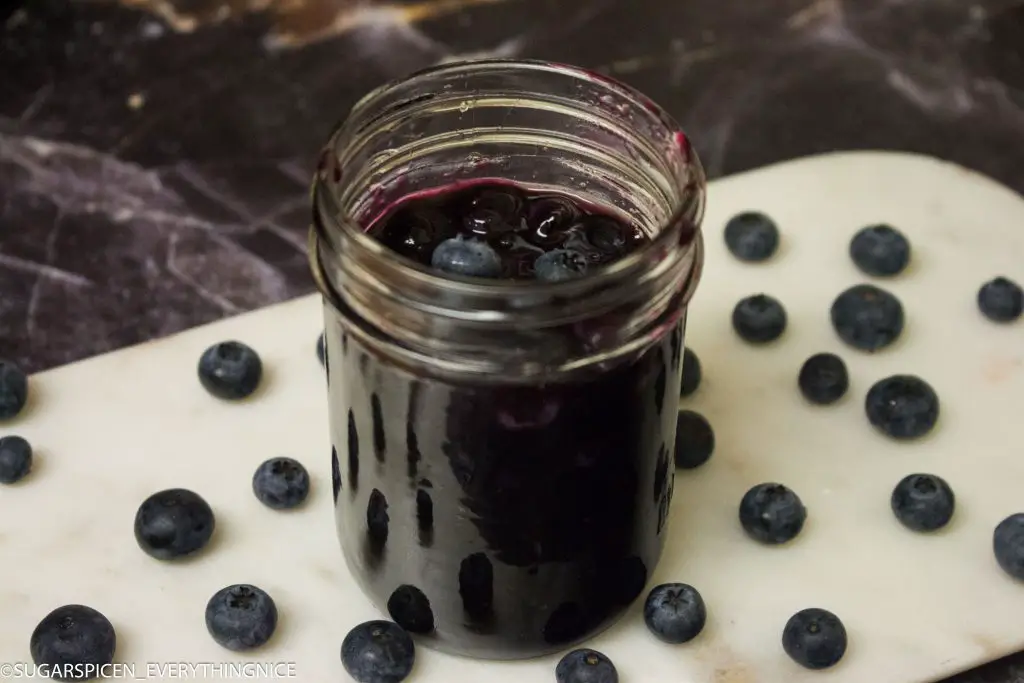 Blueberry topping sauce in a mason jar and lot of blueberries around it