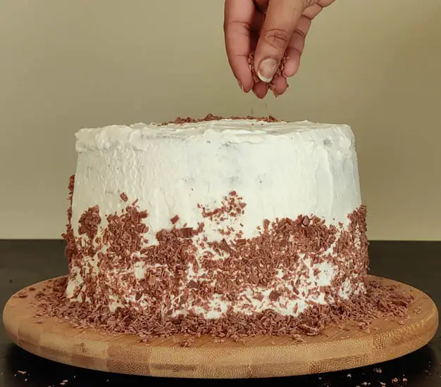 adding chocolate shavings halfway up the cake and on top