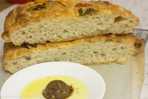Cut Focaccia bread with air pocket. Herb and olive oil mixture kept in front.