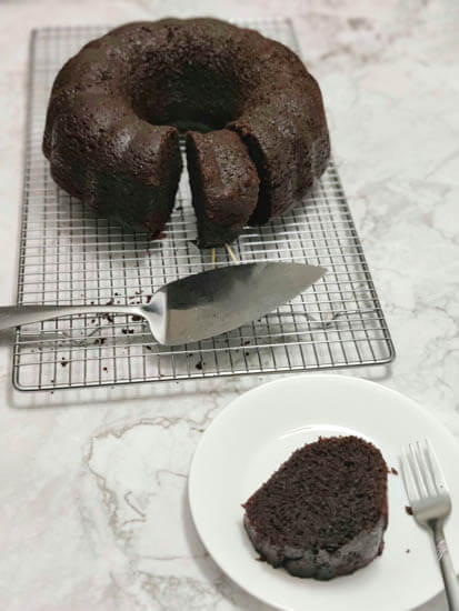 vegan rum cake on a wire rack with a piece cut off on a white plate