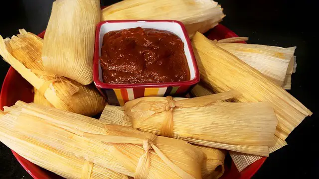 tamales kept on a plate around a cup of salsa