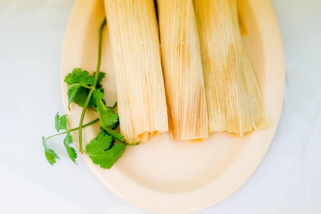 4 tamales with husk kept on a plate