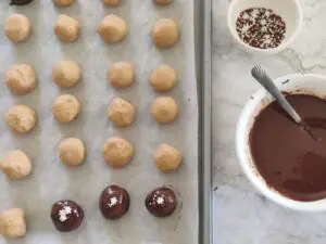 peanut butter bon bons covered in chocolate and placed on tray with parchment paper