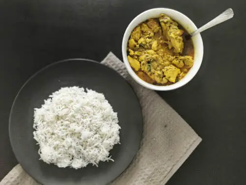a plate of white basmati rice and a side of chicken salan kept on a bowl