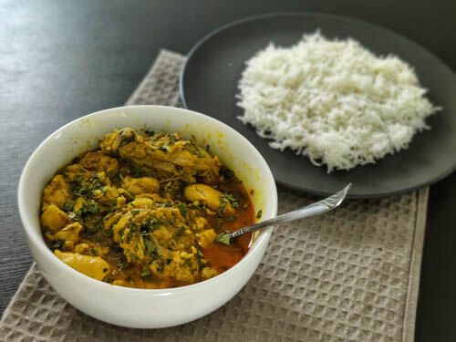 chicken salan in a white bowl with a spoon with a side of white rice