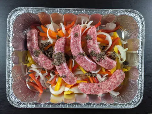 raw brats on top of peppers and onion with vinaigrette on top
