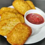 air fryer hash browns in a white plate with a side of ketchup in a small bowl