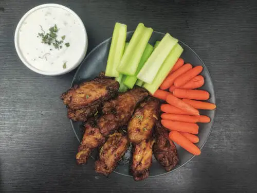 frozen air fryer chicken wings served on plate with carrots and celery and ranch kept on the side.