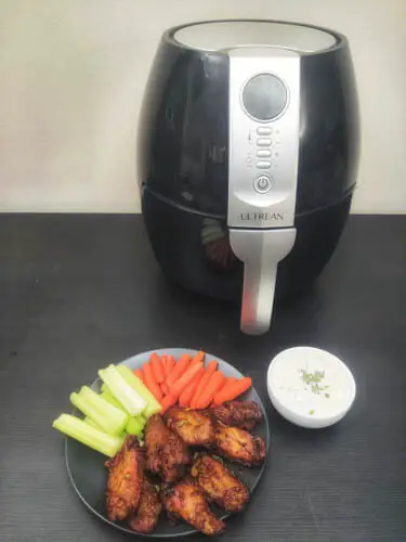 frozen air fryer chicken wings served on plate with carrots and celery with air fryer in the background