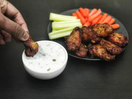 frozen air fryer chicken wings served with carrots, celery and ranch and chicken wing being dipped in eggless ranch