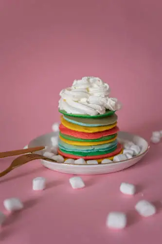 colorful stack of pancakes with a big dollop of cool whip on top and marshmellows scattered around it.