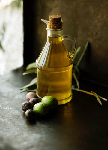 olive oil in a glass container with olive kept on the side