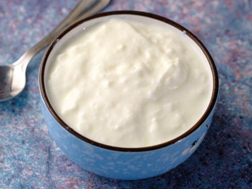 plain yogurt in a blue bowl with spoon on the side