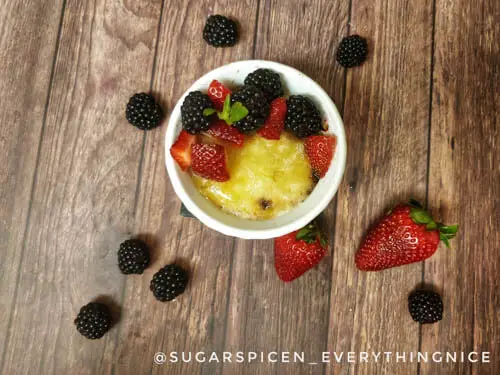 top view photo of eggless creme brulee in a white ramekin with strawberries and blackberries on top. 