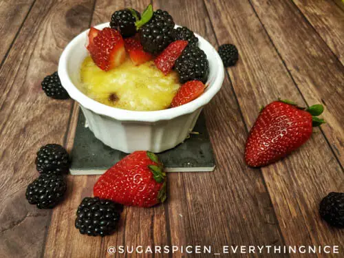 eggless creme brulee in a white ramekin with strawberries and blackberries on top