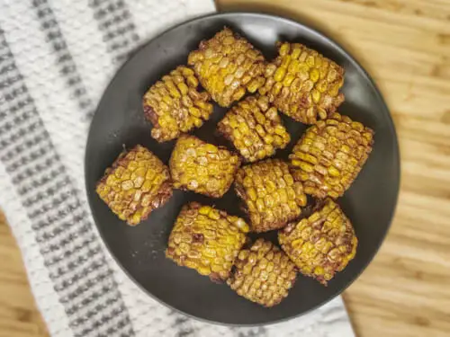 top shot of deep fried corn with cajun seasoning on a black plate over white kitchen towel