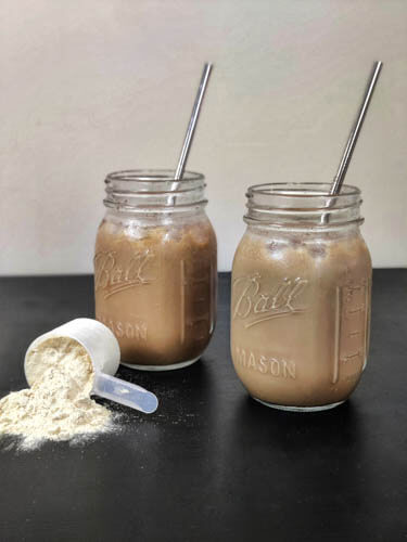 2 mason jars filled with coffee and protein mixed drink and protein powder in a scoop kept in front of it