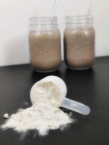 vegan protein powder in the front falling from the scoop