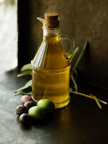 olive oil in a glass jar with olives kept on the side