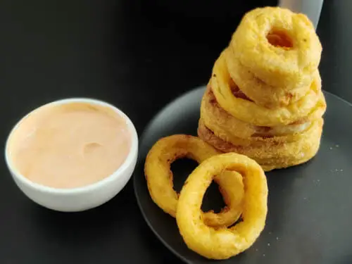 air fryer frozen onion rings are stacked one on top of the other, A side of chipotle sauce is kept on the side