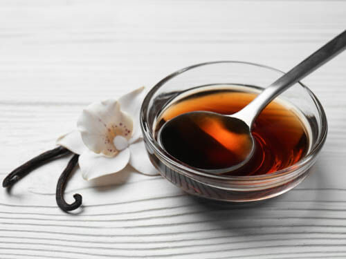pure vanilla extract in a glass bowl with vanilla bean and vanilla flower in the background