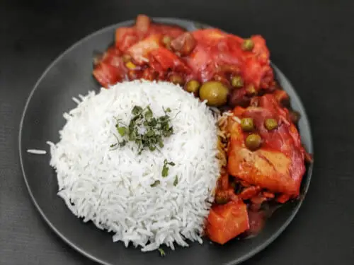 cuban chicken fricassee served with white rice on a black plate