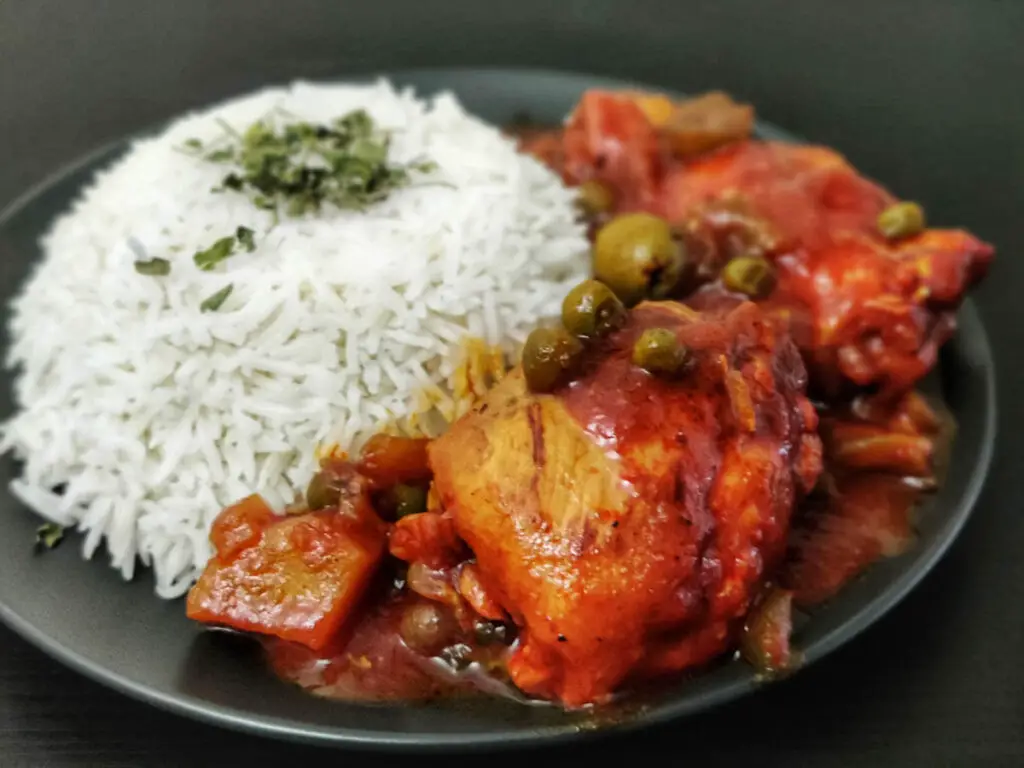 cuban chicken fricassee served with white rice on a black plate