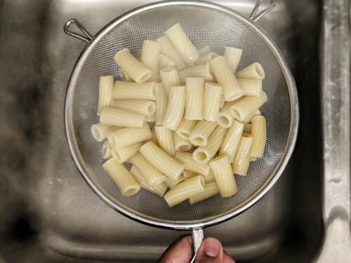 cooked pasta in strainer held over the sink