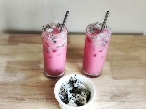 Dragon Drink in a tall glass, one kept side by side with a bowl of dragon fruits kept in front of them. Photo taken from an upward angle