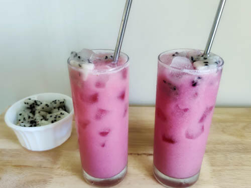 Dragon Drink in a tall glass, one kept side by side with a bowl of dragon fruits kept in front of them. Photo taken from an upward angle