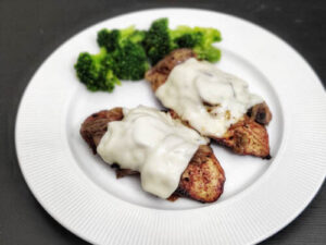 Smothered Chicken Texas Roadhouse (Copycat Recipe) two chicken breast smothered in jack cheese kept on a white plate with a side of broccoli
