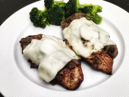 two chicken breast smothered in jack cheese kept on a white plate with a side of broccoli